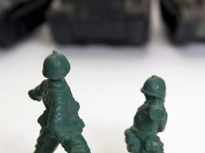 Green toy soldiers fighting black tanks