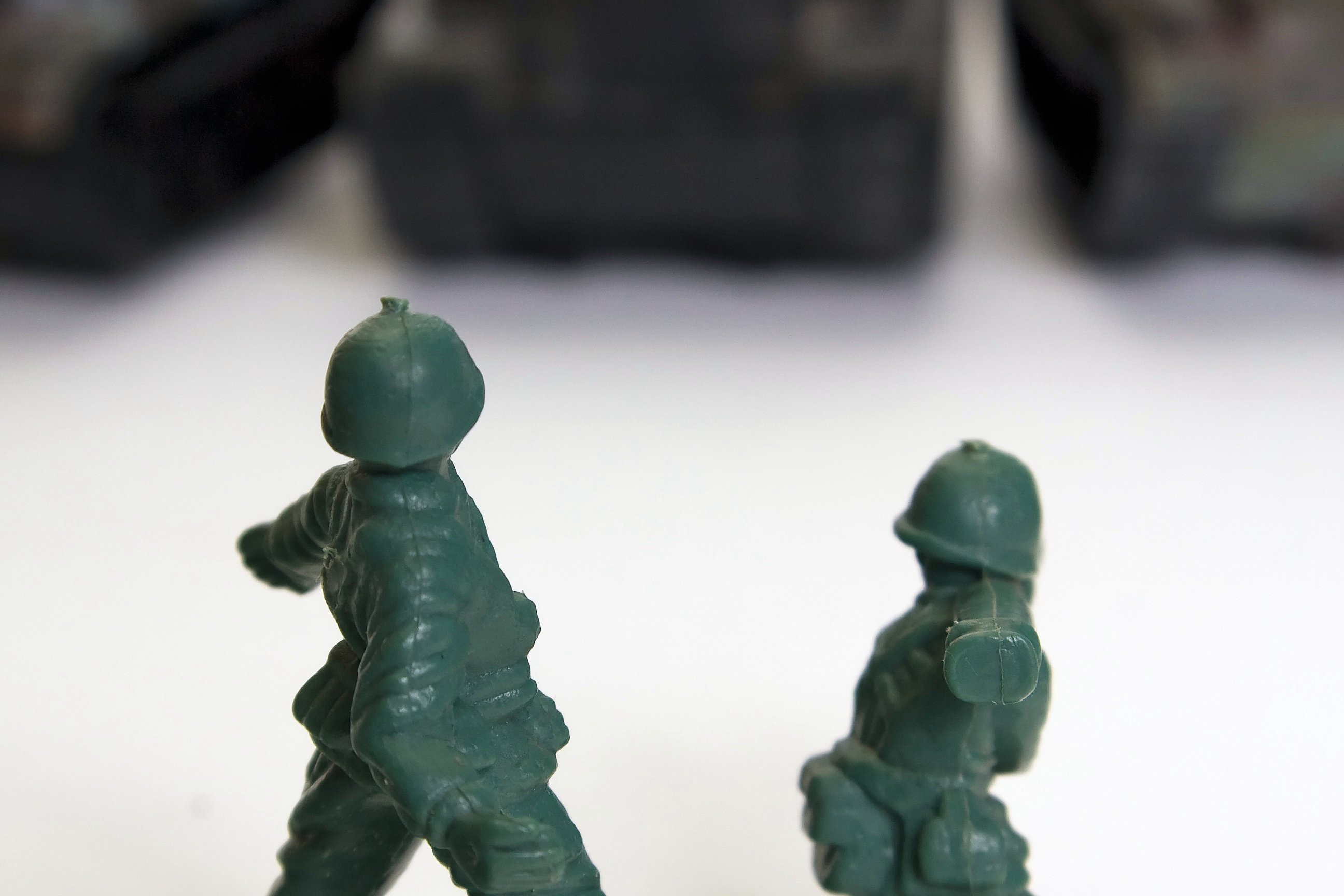 Green toy soldiers fighting black tanks
