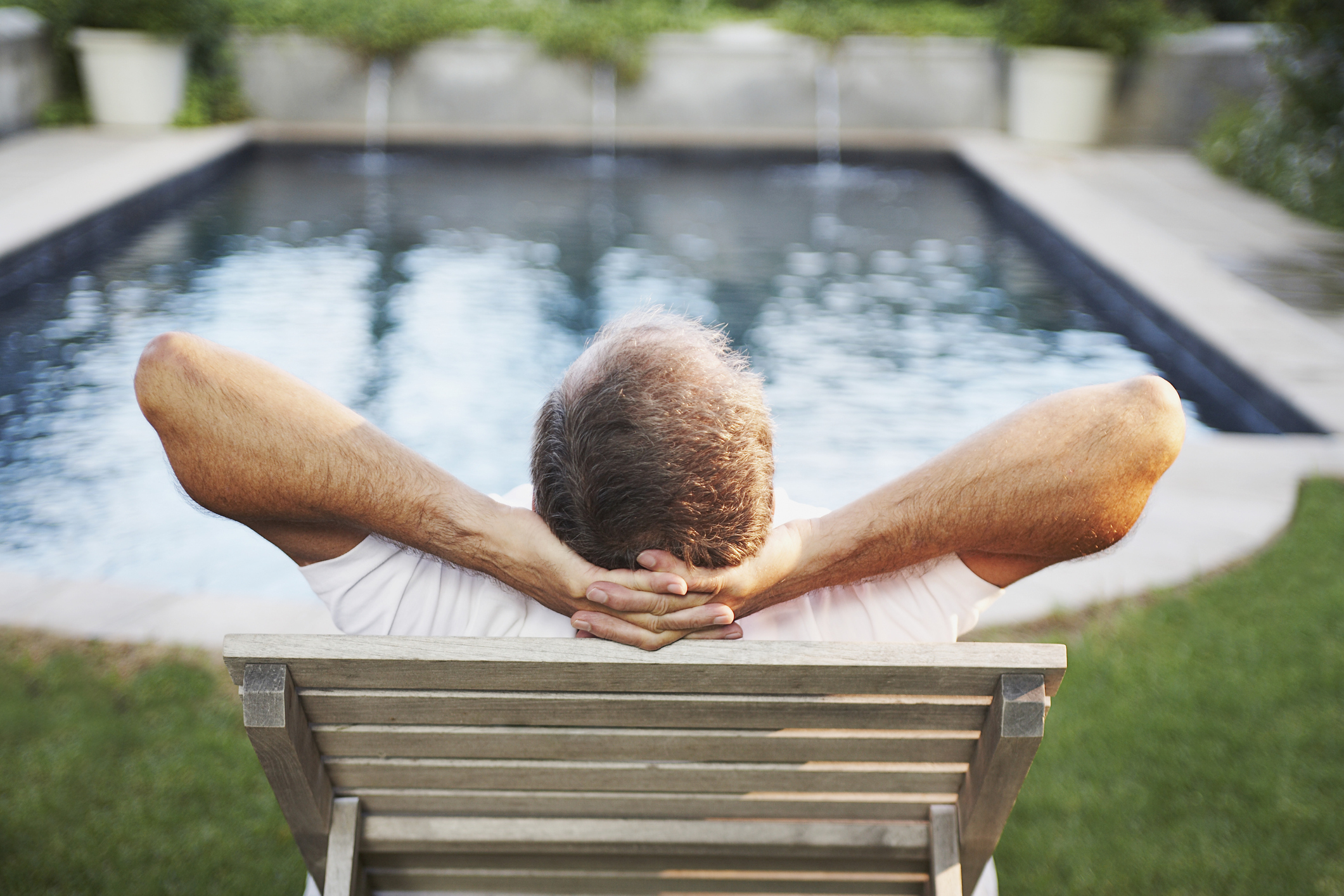 Man sitting with hands behind head admiring swimming pool