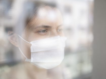 Young woman in quarantine looking through the window