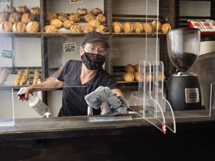 Bakery owner wiping down surfaces wearing mask.