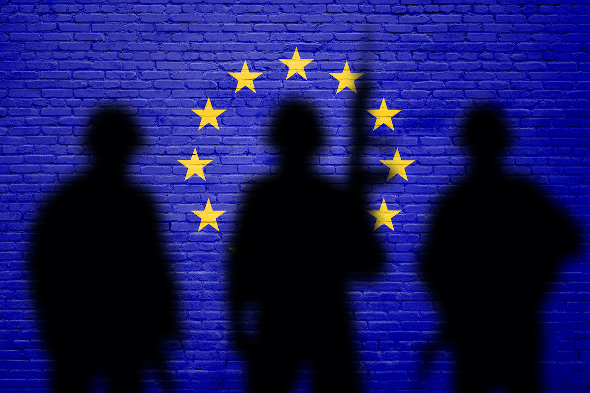 Flag of Europe Union painted on a brick wall with soldiers shadows. War concept