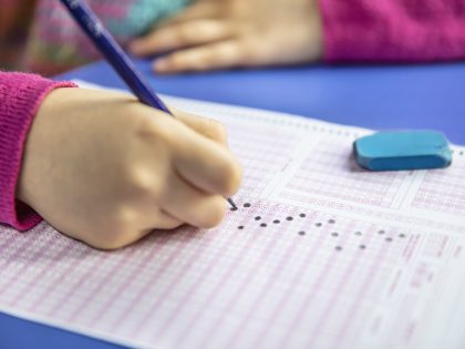 hand student testing in exercise and taking fill in exam carbon paper computer sheet with pencil at school test room, education concept
