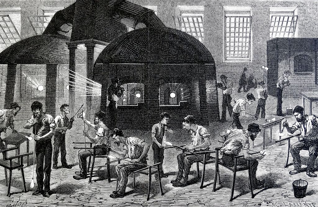 General view of a glassworks, showing men engaged in the various stages of making drinking glasses.