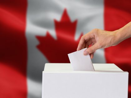 Close-up of human hand casting and inserting a vote and choosing and making a decision what he wants in polling box with Canada flag blended in background