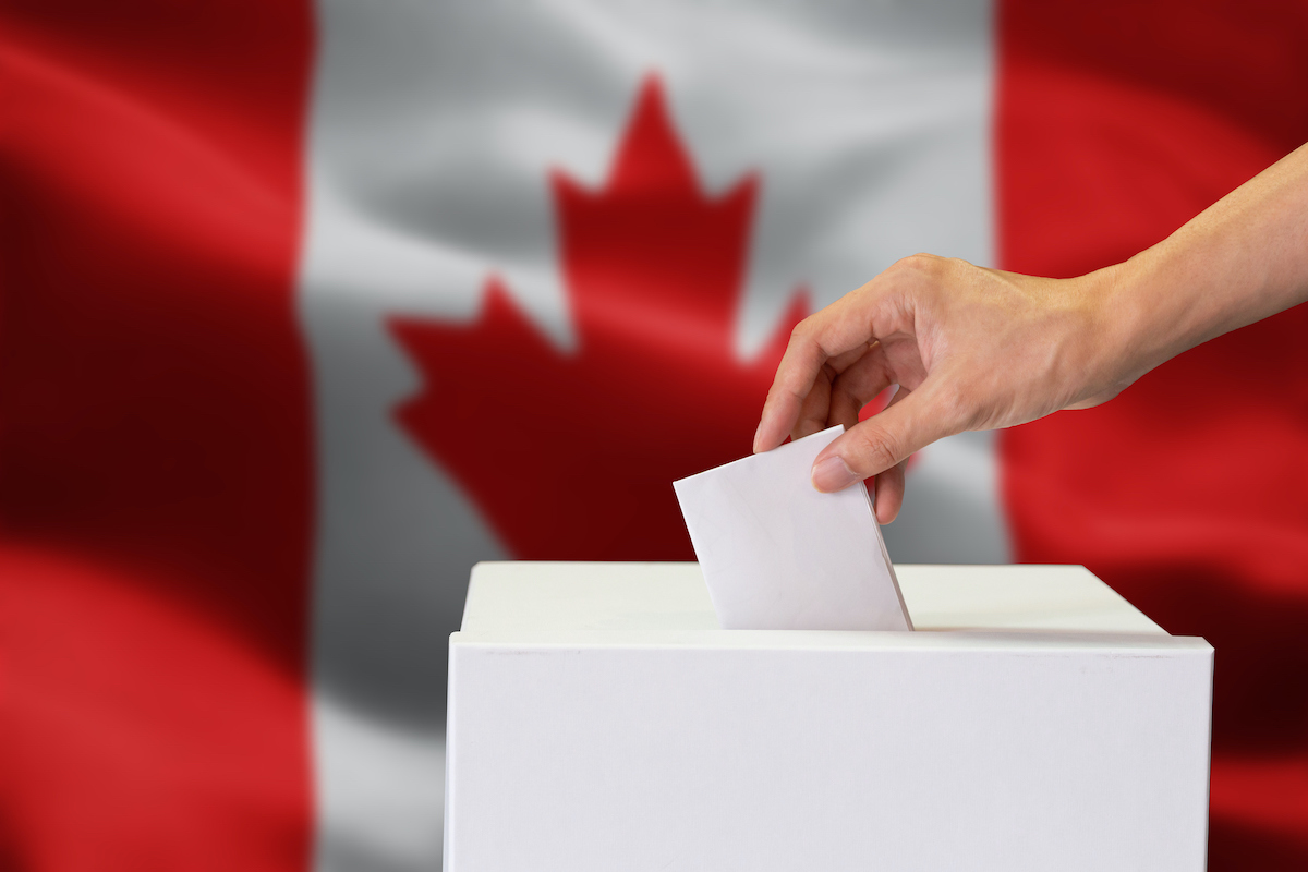 Close-up of human hand casting and inserting a vote and choosing and making a decision what he wants in polling box with Canada flag blended in background