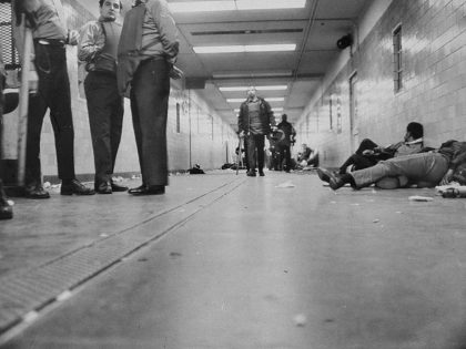 Prisoners sit handcuffed on ground along hallway after riots