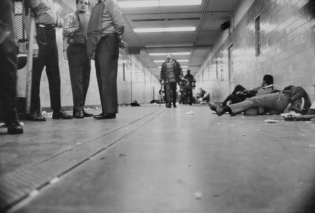 Prisoners sit handcuffed on ground along hallway after riots