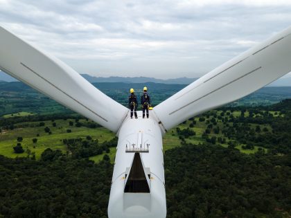 Two Electric engineer wearing Personal protective equipment working  on top of wind turbine farm.