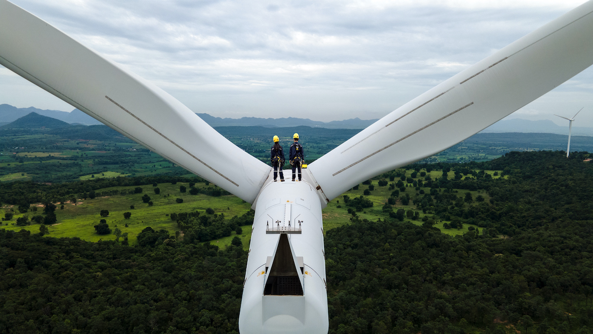 Two Electric engineer wearing Personal protective equipment working  on top of wind turbine farm.