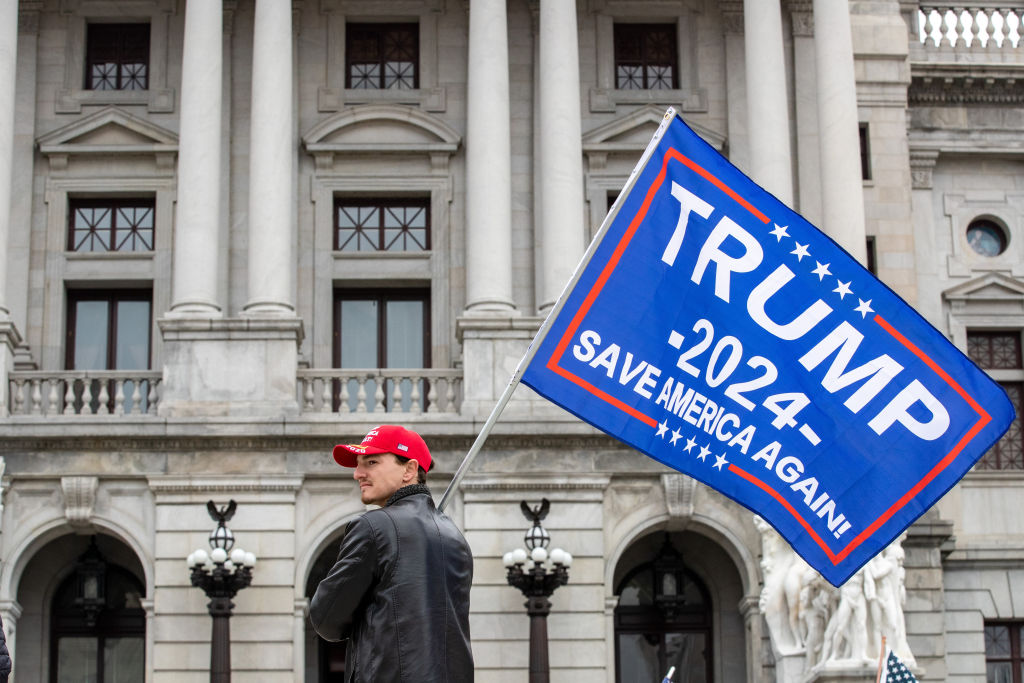 A protester holds a Trump 2024 flag in front of the