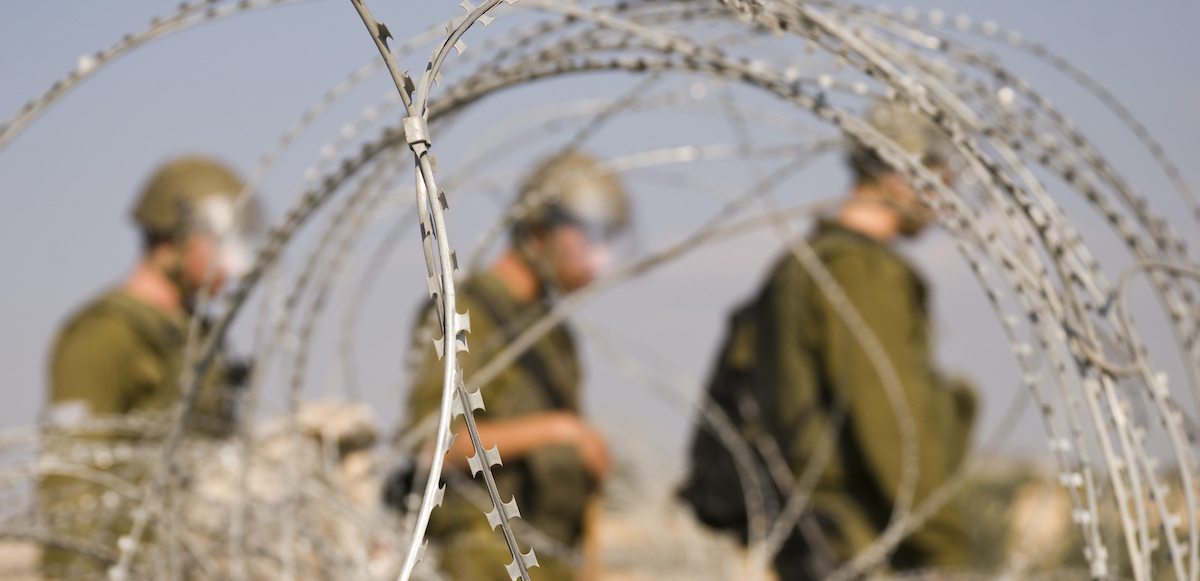 Israeli soldiers behind razor wire in the West Bank