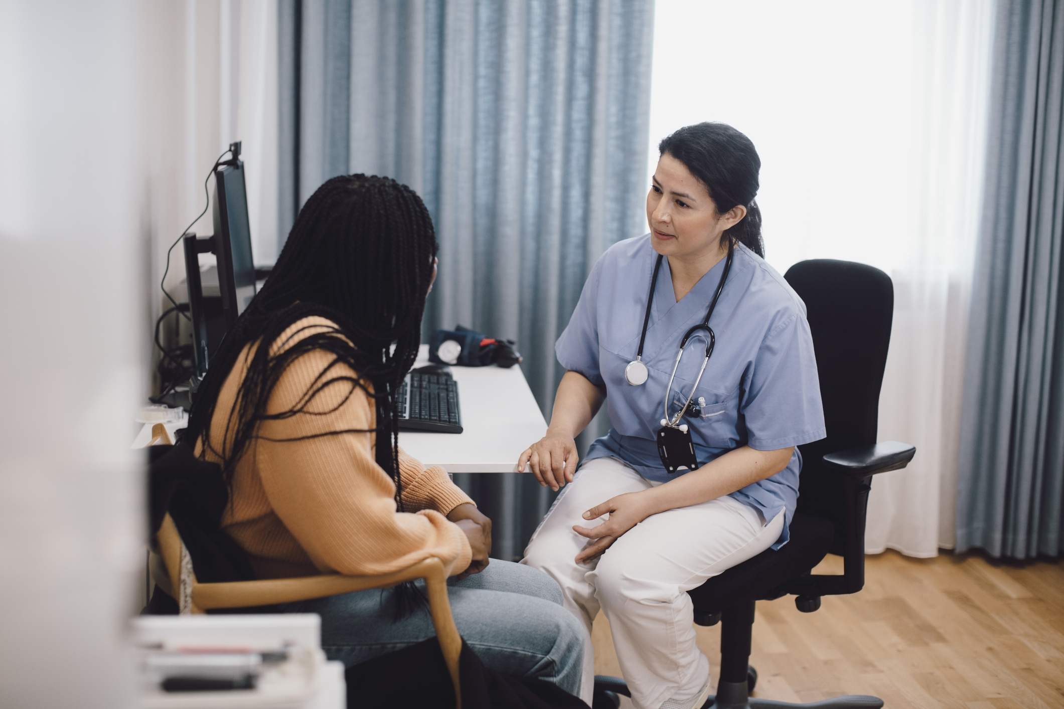 Female doctor giving advice to woman while sitting in medical clinic