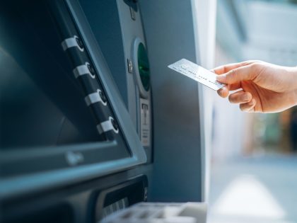 Close up of female hand inserting her bank card into automatic cash machine in the city. Withdrawing money, paying bills, checking account balances and make a bank transfer. Privacy protection, internet and mobile banking security concept