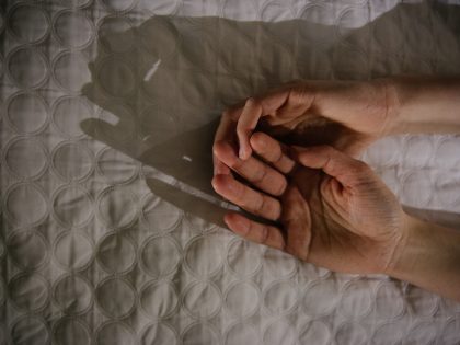 Close-Up Of Hands On Bed