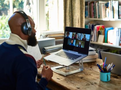 Black entrepreneur wearing headphones on video conference call on laptop in home office