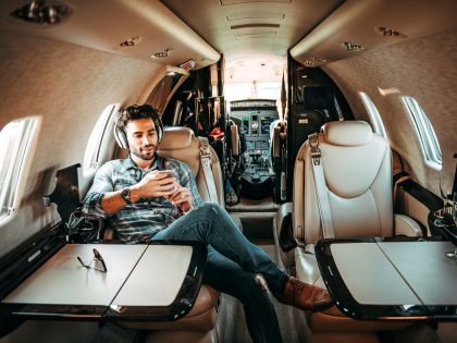 Young rich man listening to music over the headphones and using a mobile phone while sitting in a private jet