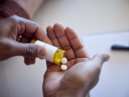 African American man pouring medications out of a bottle into his hand.