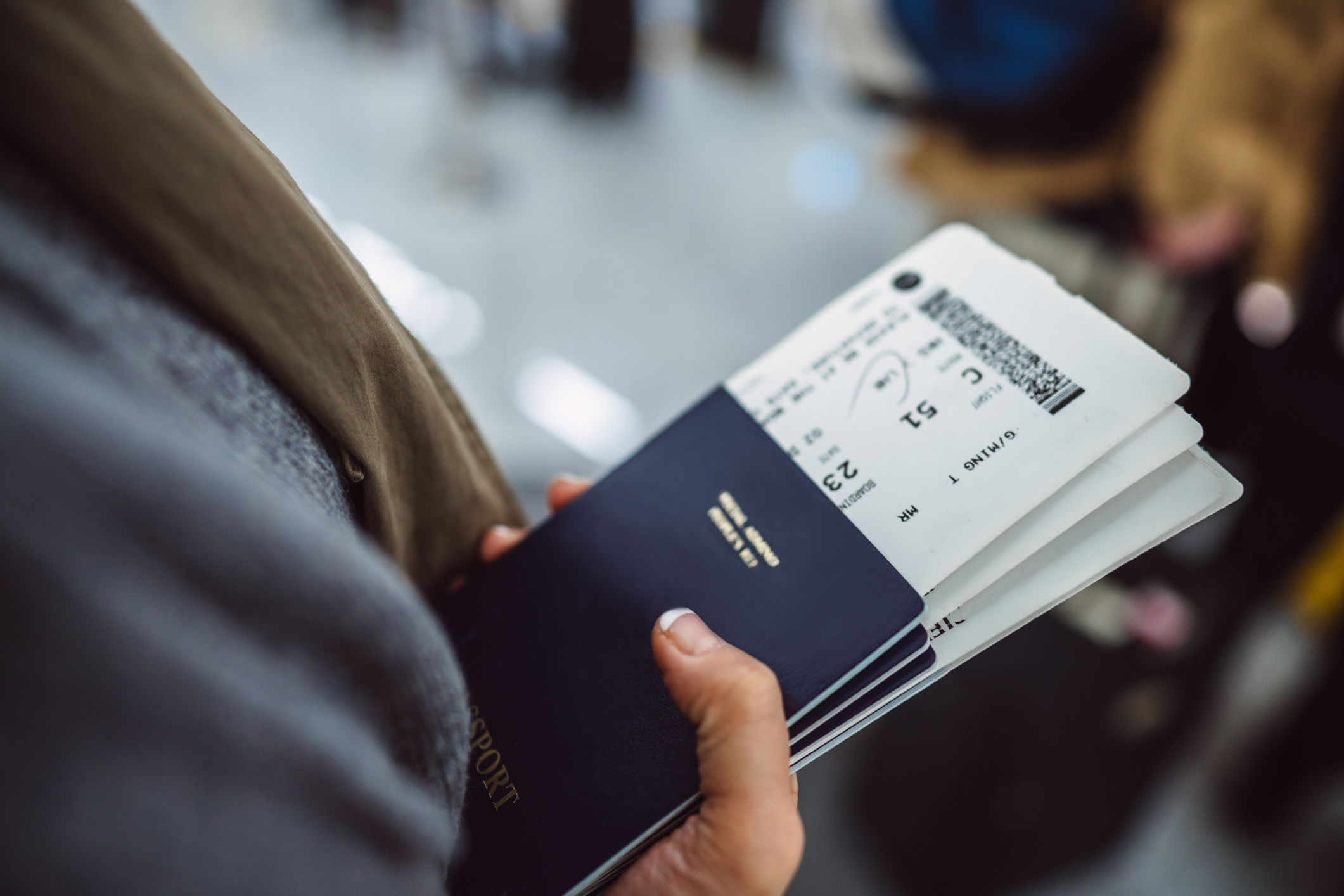 Woman’s hands holding passports &amp;amp; boarding passes of her family while waiting at the check-in counter in the airport