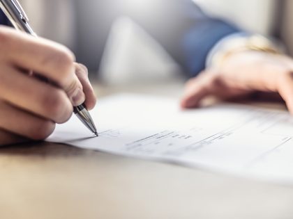 A businessman's hand signs an invoice, loan, car leasing or other document.