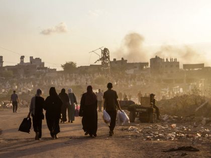 Palestinians walk along a street which was bombed by the