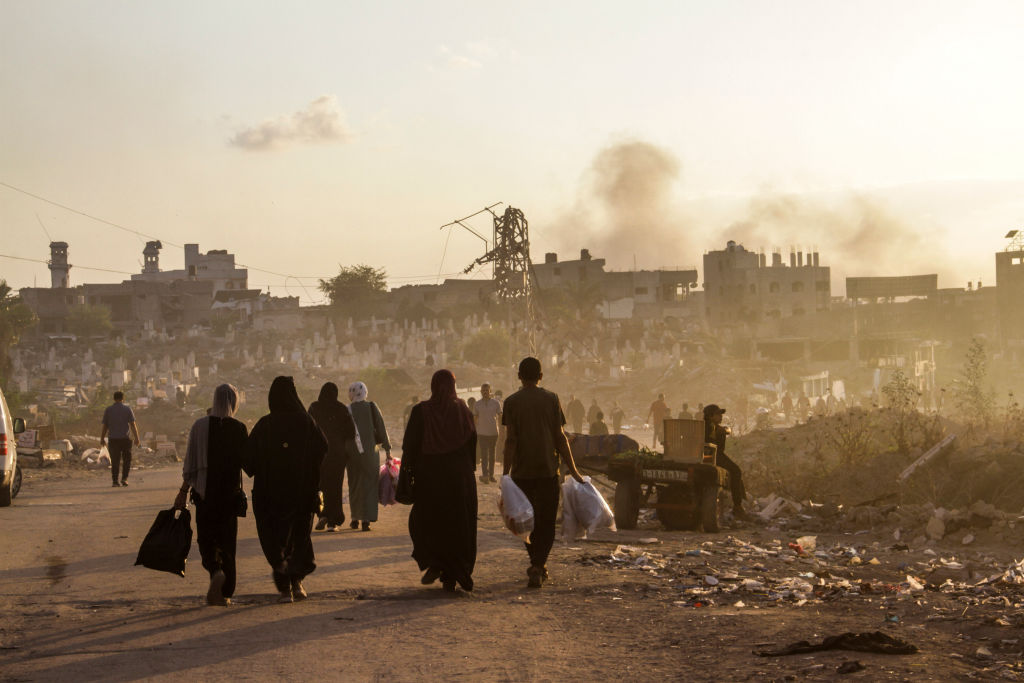 Palestinians walk along a street which was bombed by the