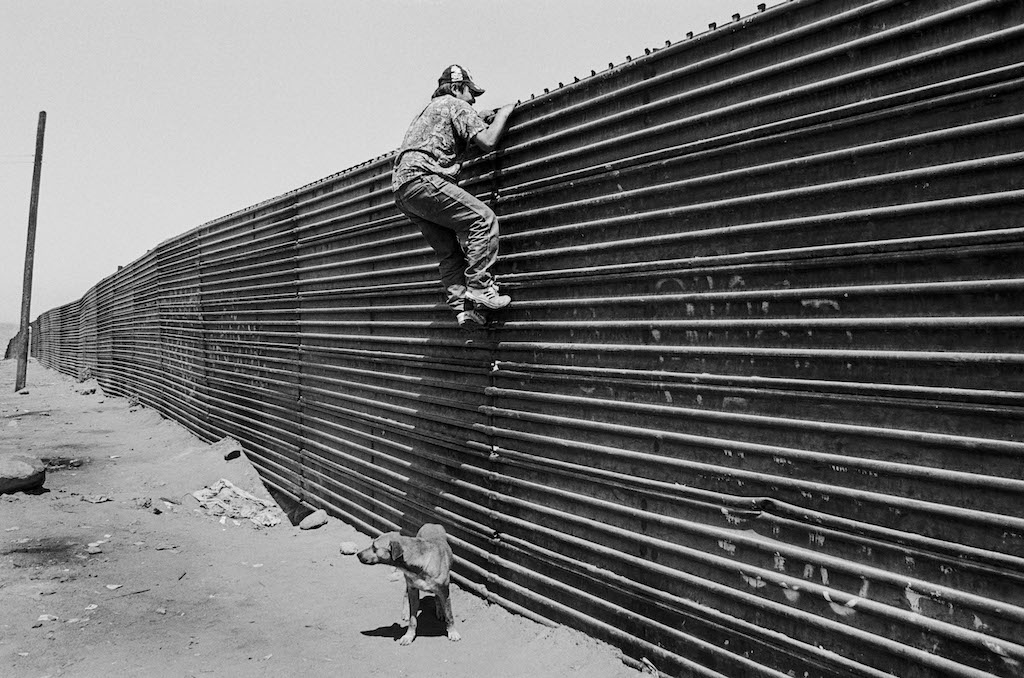 A Migrant Looks Over the Wall at the U.S. Mexico Border