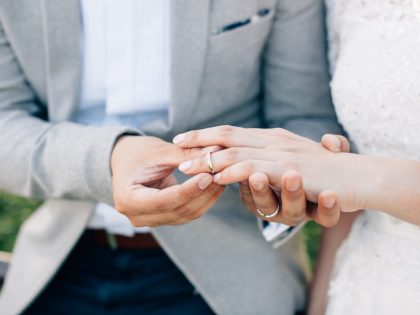 Groom putting ring on bride's finger. Rings exchange. Happy couple celebrating wedding outdoors.