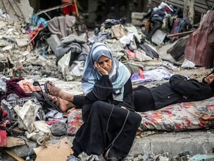 A woman sits next to a man lying on a mattress amid destruction following an Israeli air strike in Nuseirat in the central Gaza Strip on October 23, 2026.