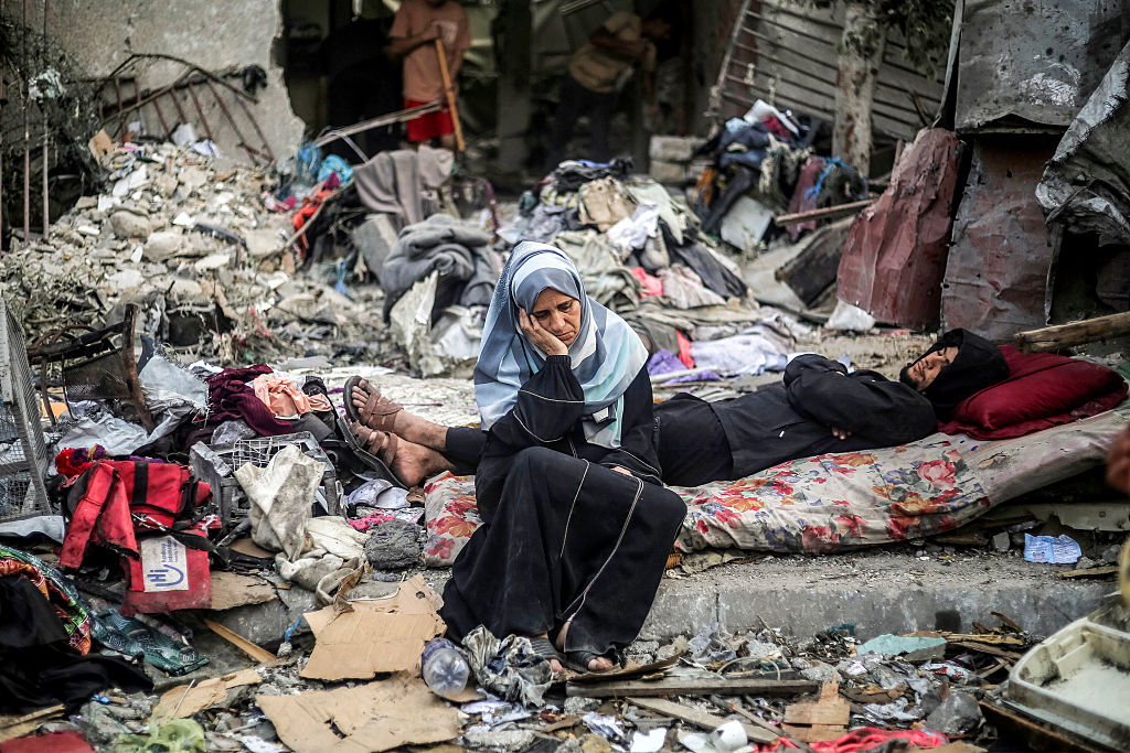 A woman sits next to a man lying on a mattress amid destruction following an Israeli air strike in Nuseirat in the central Gaza Strip on October 23, 2026.