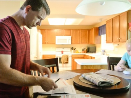 A man pays bills in a dining area while his daughter eats.