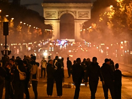 Protesters gather on the Champs-Élysées in Paris with the Arc de Triomphe in the background.