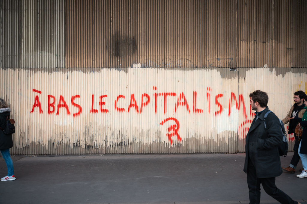 Demonstrators walk in front of a red tag saying ''Down with capitalism'' accompanied by the hammer-and-sickle symbol during a demonstration in Paris on February 16, 2023.