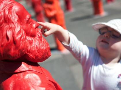 A small girl touches a red Karl Marx figure.
