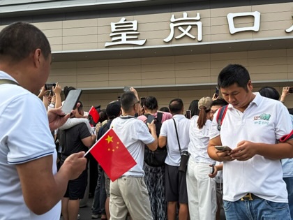 Two men look at their smartphones as people gather and take photos outside the redeveloped Huanggang Port on October 12, 2026, in Shenzhen.