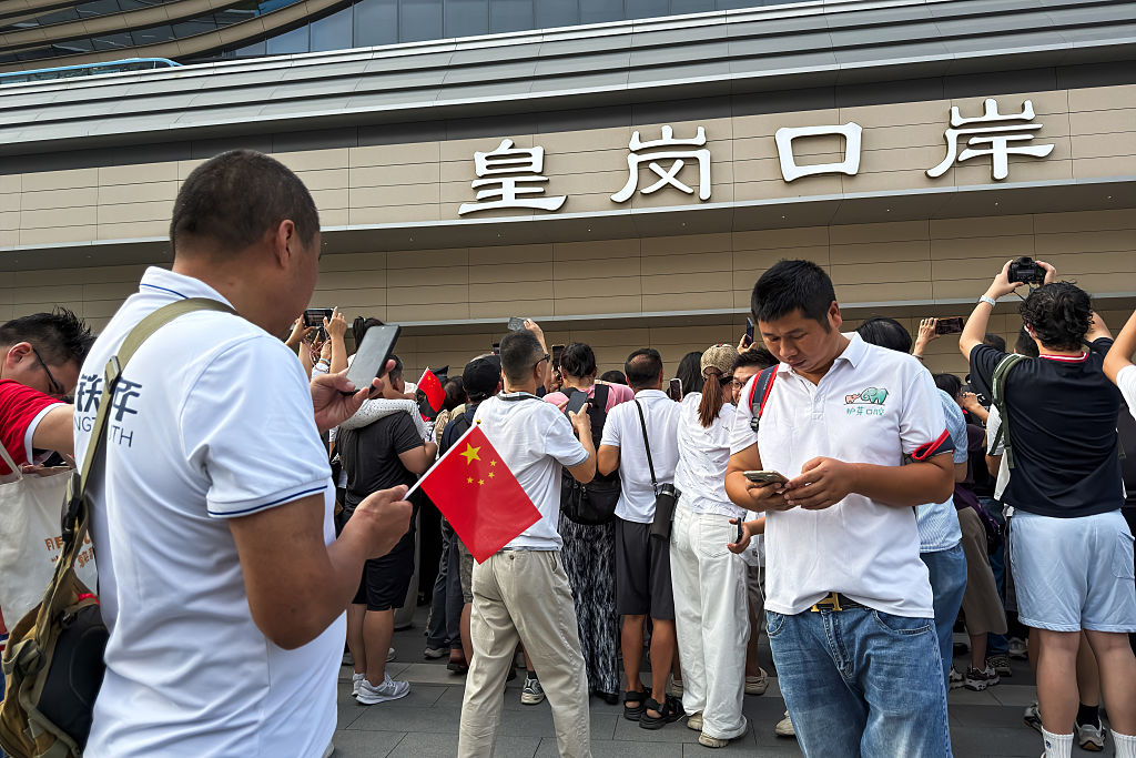 Two men look at their smartphones as people gather and take photos outside the redeveloped Huanggang Port on October 12, 2026, in Shenzhen.