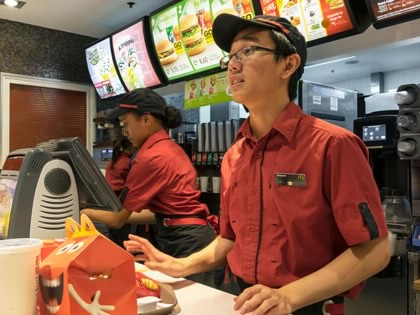 A young McDonald’s worker stands behind the counter at a McDonald’s restaurant with a tray with an order of food on it.