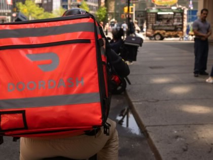 A delivery driver biking on a street with a DoorDash bag on his back.