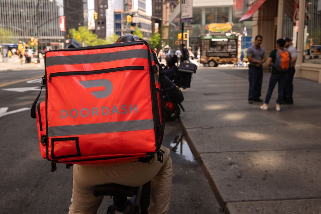 A delivery driver biking on a street with a DoorDash bag on his back.