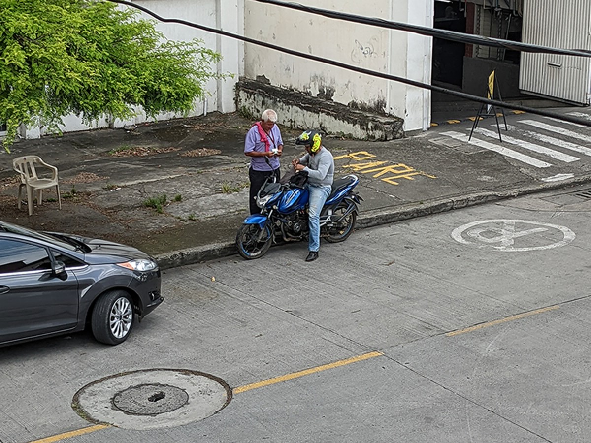 A gota a gota debt collector on a motorcycle, with his helmet on, talks to another man on the streets of Cali, Colombia.