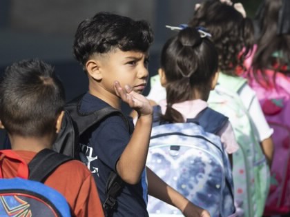 An elementary-aged student turns and waves as he walks in a line with other children.