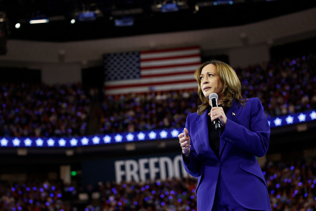 Kamala Harris speaking into a microphone with a stadium full of people and a sign that says "Freedom" behind her.