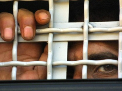 A Palestinian prisoner being transferred, looking through the fencing of a bus. 
