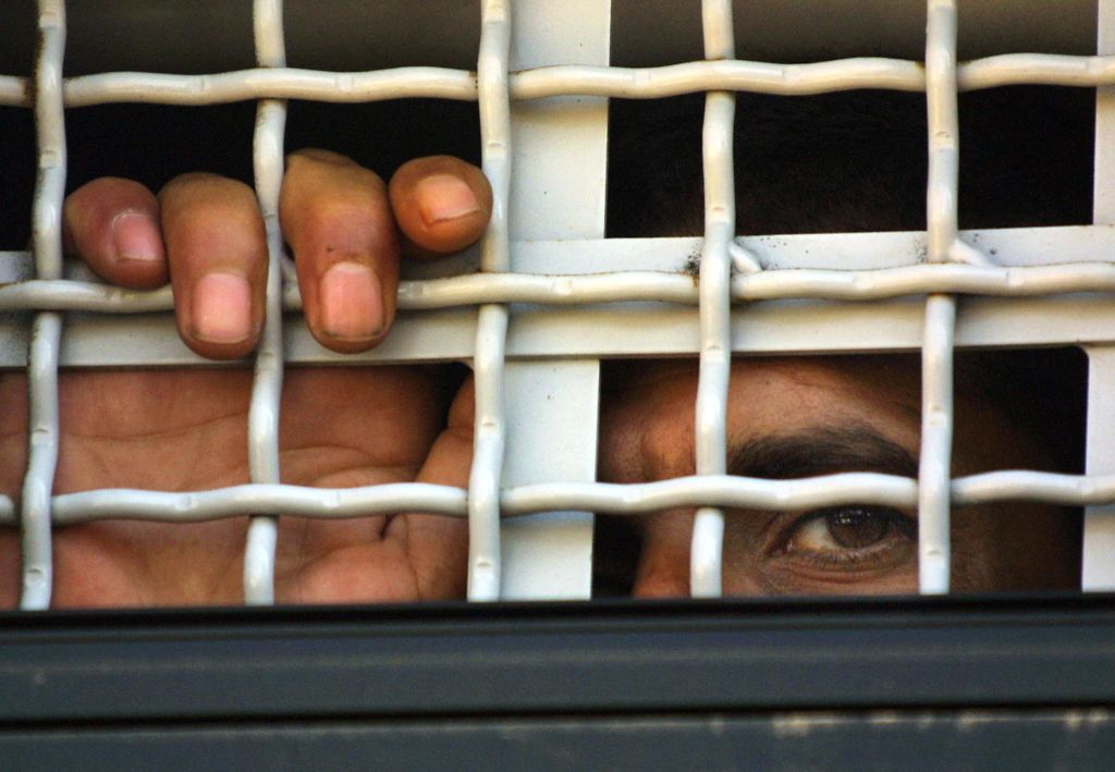 A Palestinian prisoner being transferred, looking through the fencing of a bus. 