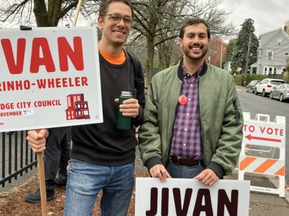 Jivan Sobrinho-Wheeler stands with a supporter, both holding campaign signs for Jivan. 