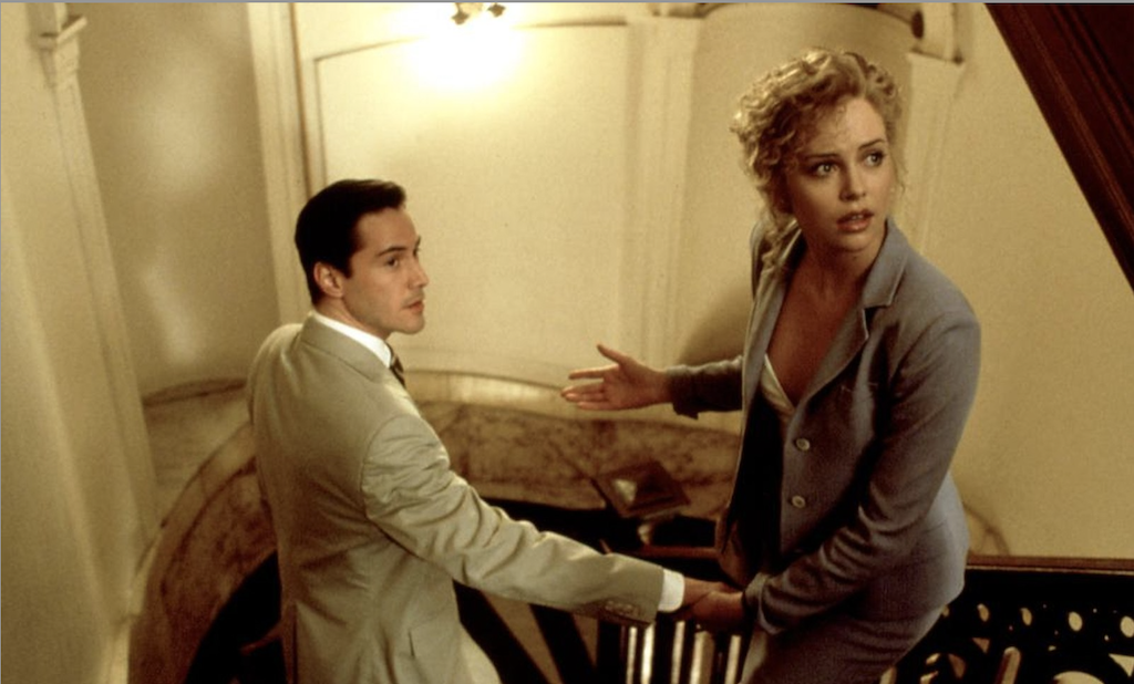Still from The Devil's Advocate of Keanu Reeves's character and Charlize Theron's character holding hands and walking down a staircase.