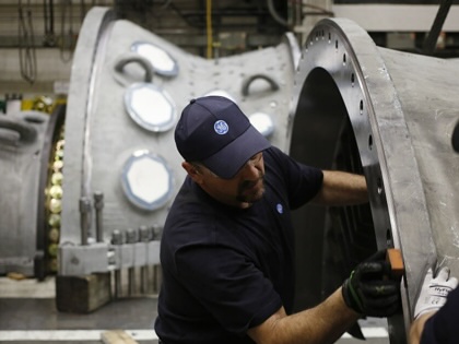 A man works on large metal machinery as another worker looks on.