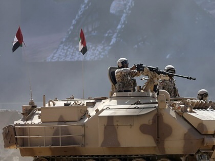 Emirati armed forces personnel in a battle tank with guns drawn and UAE flags in the background.
