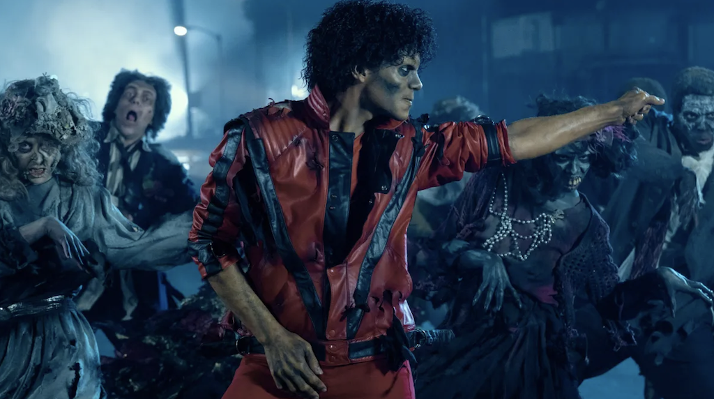 Actor Jaafar Jackson portraying Michael Jackson perfoming with a red jacket zombie-like makeup on, jestering with his right arm.