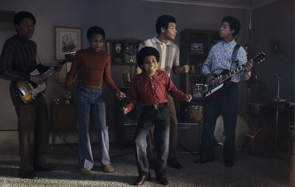 Actors portraying members of the band Jackson 5 in a living room with two playing guitars.